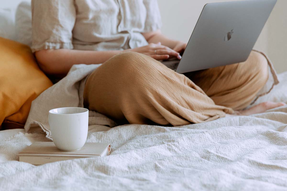 Person lounging with laptop and cup of tea on the bed